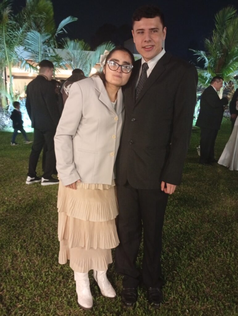 Lautaro Venturini, de traje oscuro, junto a su esposa Katherine, con saco claro y pollera larga, en un evento al aire libre.